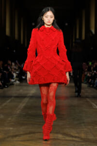 Model walking the runway in a bold red oversized knitted coat with a chunky cable pattern, paired with red lace tights and boots?
