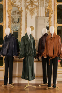 Four mannequins wear fringed leather jackets in navy, green, brown, and tan against a gilded, mirror-framed backdrop.