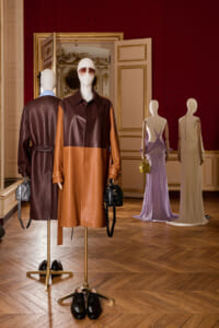Mannequins wear color‑block leather coats and handbags in a luxurious showroom with gold-trimmed doors and red wallpaper.