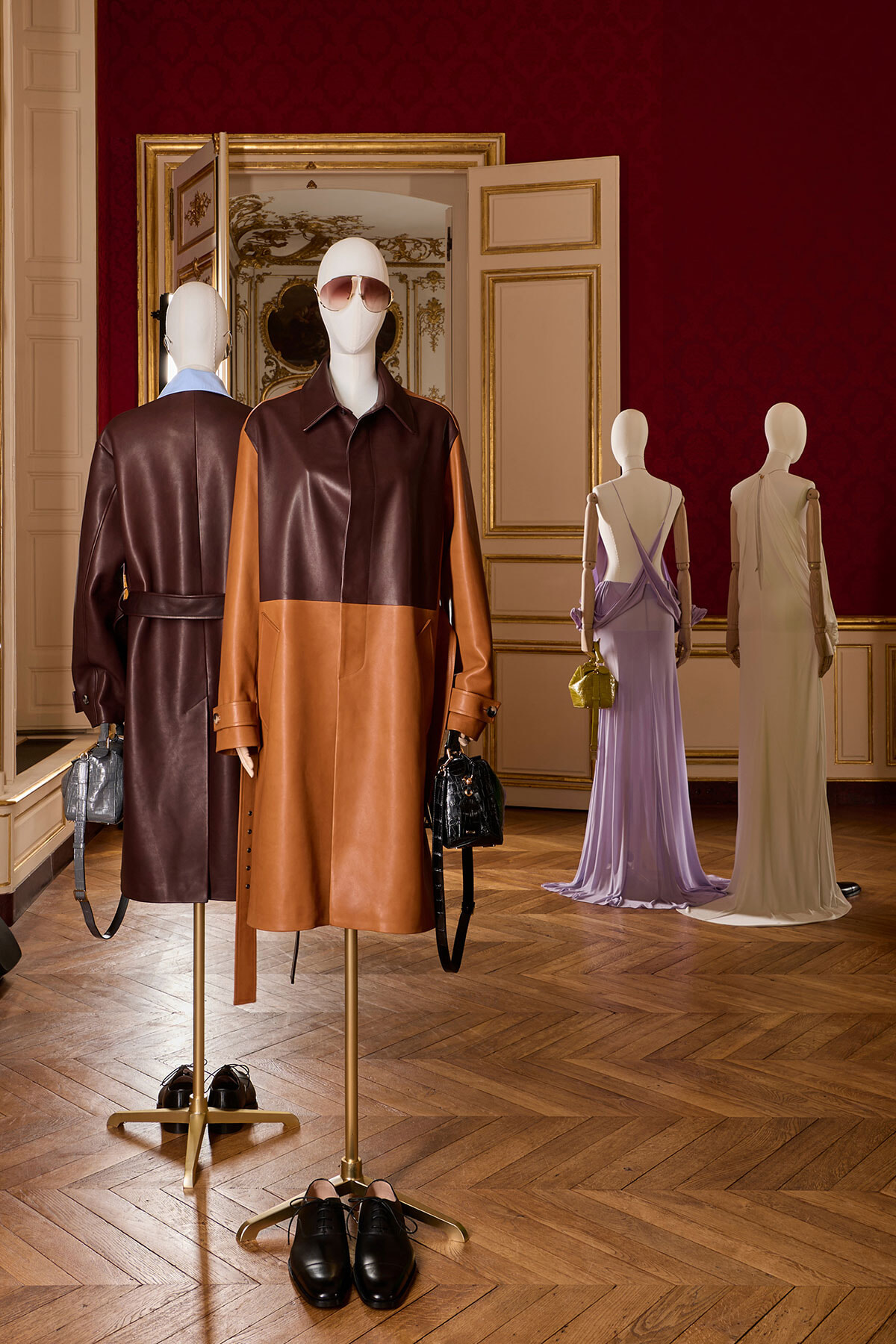 Mannequins wear color‑block leather coats and handbags in a luxurious showroom with gold-trimmed doors and red wallpaper.