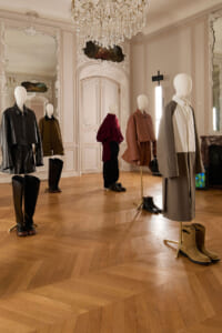Mannequins wearing stylish outfits on stands in a gilded, chandelier-lit room with mirrors and ornate detailing in the walls and doors.