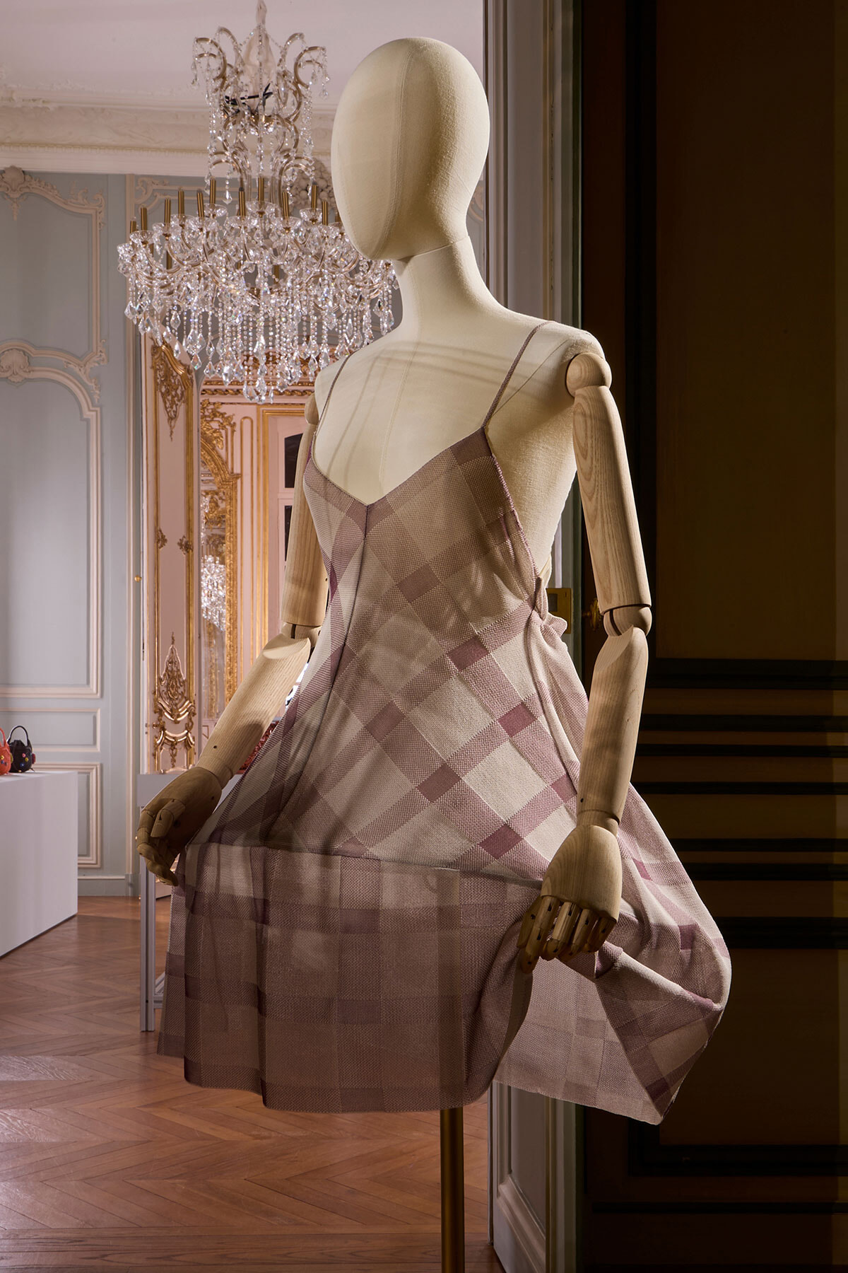 Mannequin wearing a pink plaid slip dress in a luxurious showroom with a crystal chandelier.