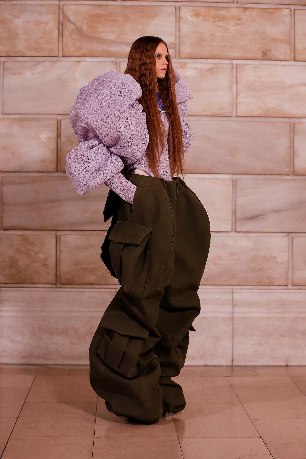 Model wearing a lavender lace top with huge puff sleeves and oversized olive cargo pants against a stone wall.