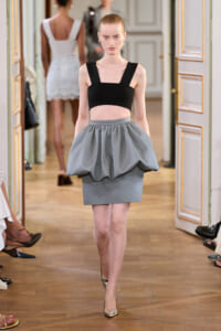 Model walks a runway wearing a black square-strap crop top and a voluminous gray bubble skirt with pointed heels.