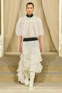 Runway look: ivory sheer blouse with puff sleeves, black sequin collar, sparkly belt, and tiered white ruffle skirt with white boots.