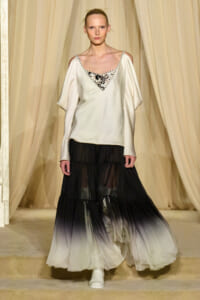 Model on runway wearing ivory satin top with beaded V-neck and a black-to-white ombre tiered skirt.