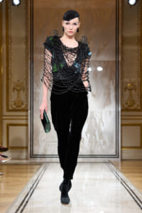 Model walks runway in black velvet pants and a densely beaded black mesh top with a glossy cap.”] ,