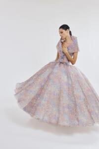 Woman in a pastel floral ball gown twirls, creating a full, flowing skirt against a light backdrop.