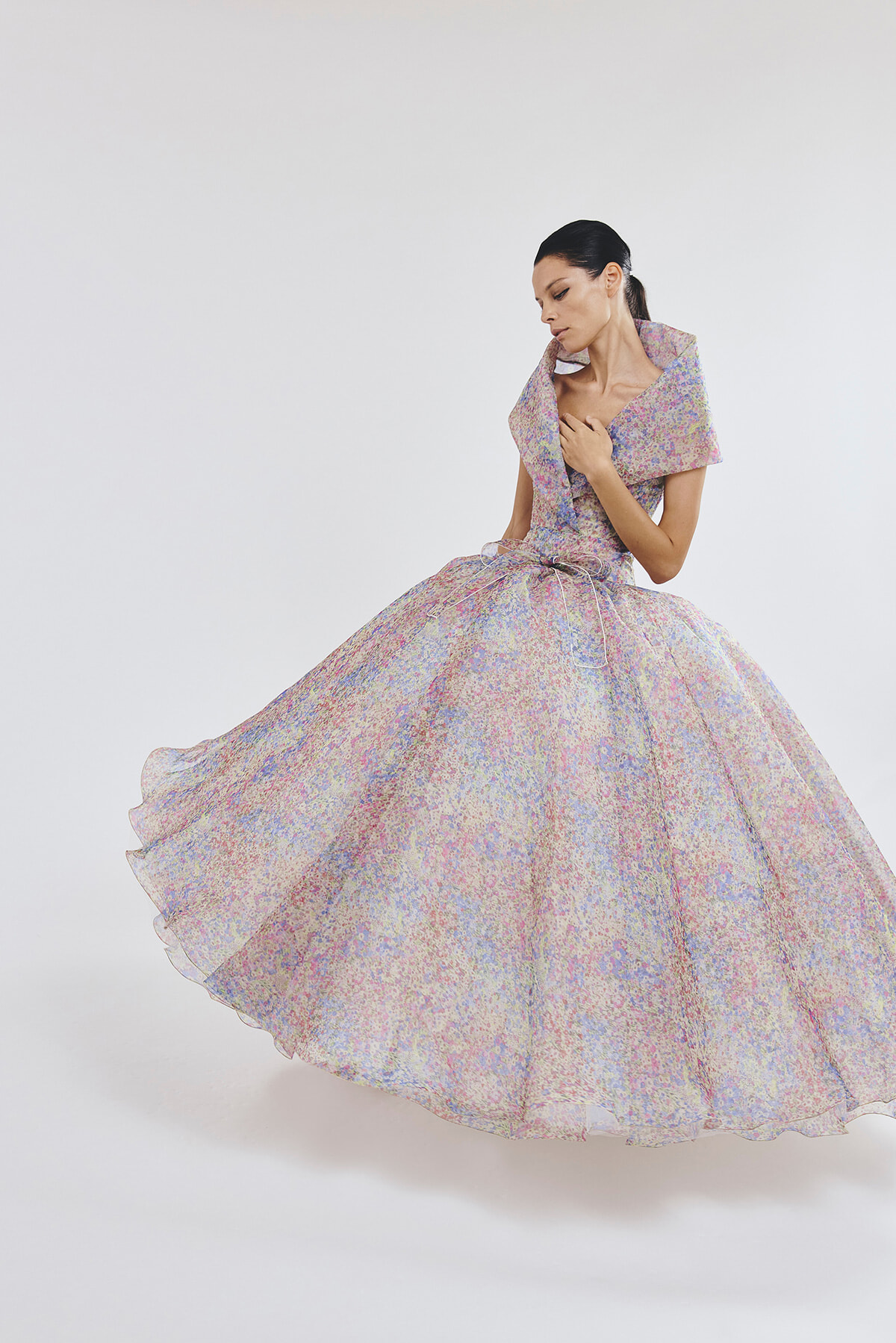 Woman in a pastel floral ball gown twirls, creating a full, flowing skirt against a light backdrop.