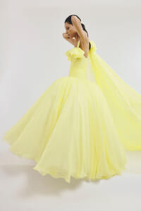Woman in a bright yellow ball gown twirls, dress flowing dramatically around her against a pale backdrop.