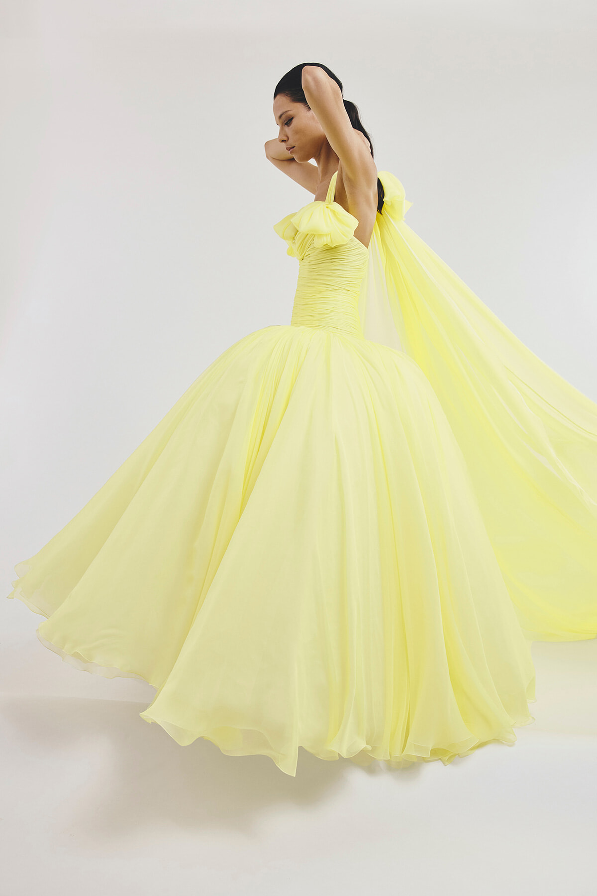Woman in a bright yellow ball gown twirls, dress flowing dramatically around her against a pale backdrop.