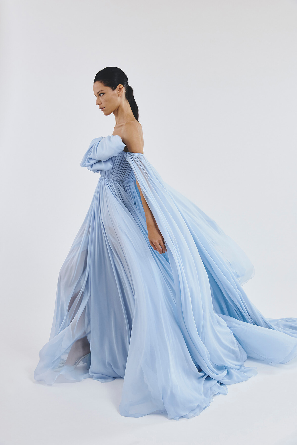 Model in a pale blue off-shoulder gown with a billowing, sheer skirt flowing to the floor and a long train.
