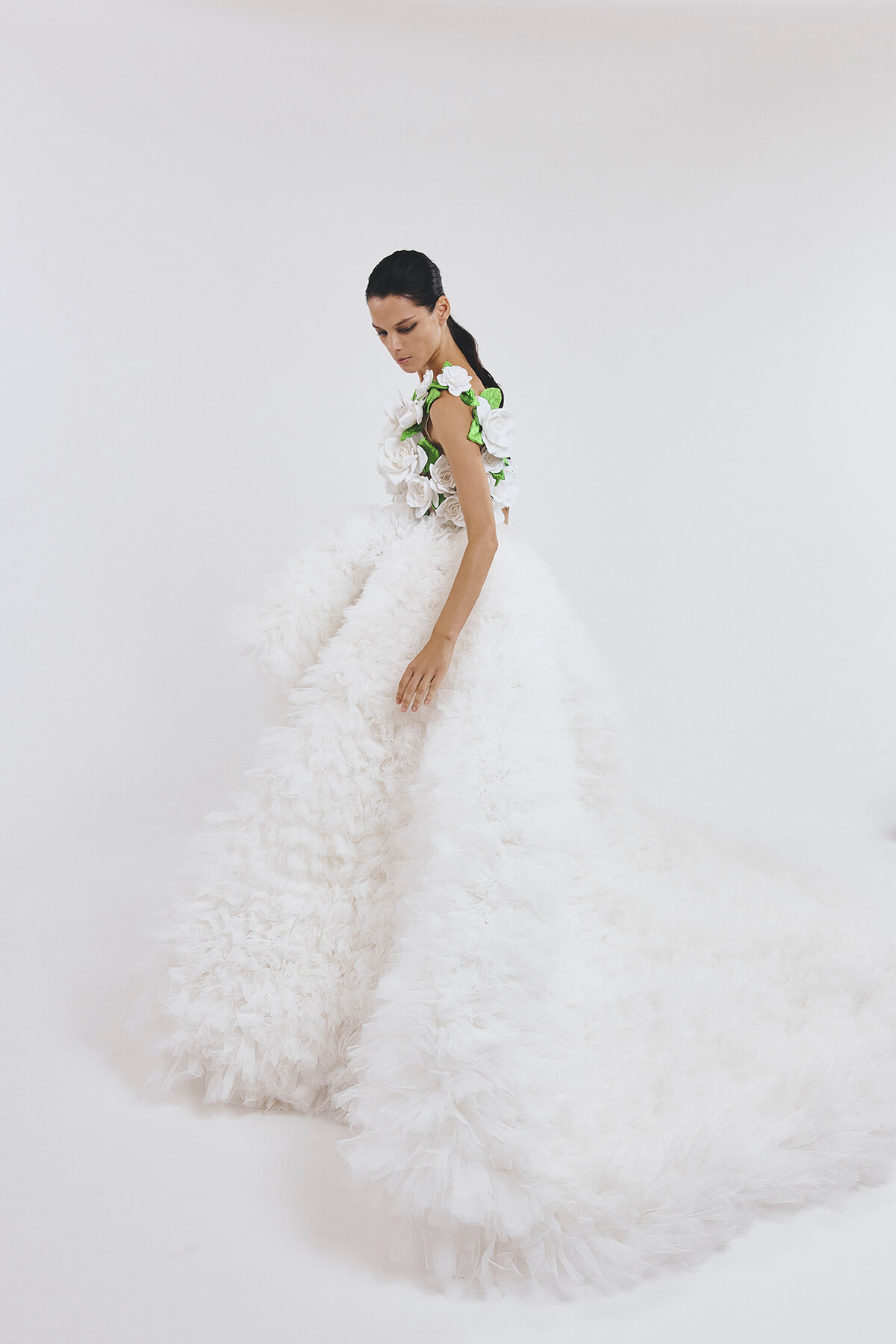 Model in a dramatic white gown with a voluminous, petal-covered skirt and a bodice made of white roses with green leaves.