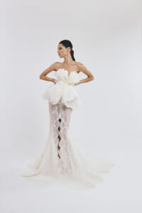 Model wearing a white lace mermaid wedding gown with an oversized floral bodice and flowing train.