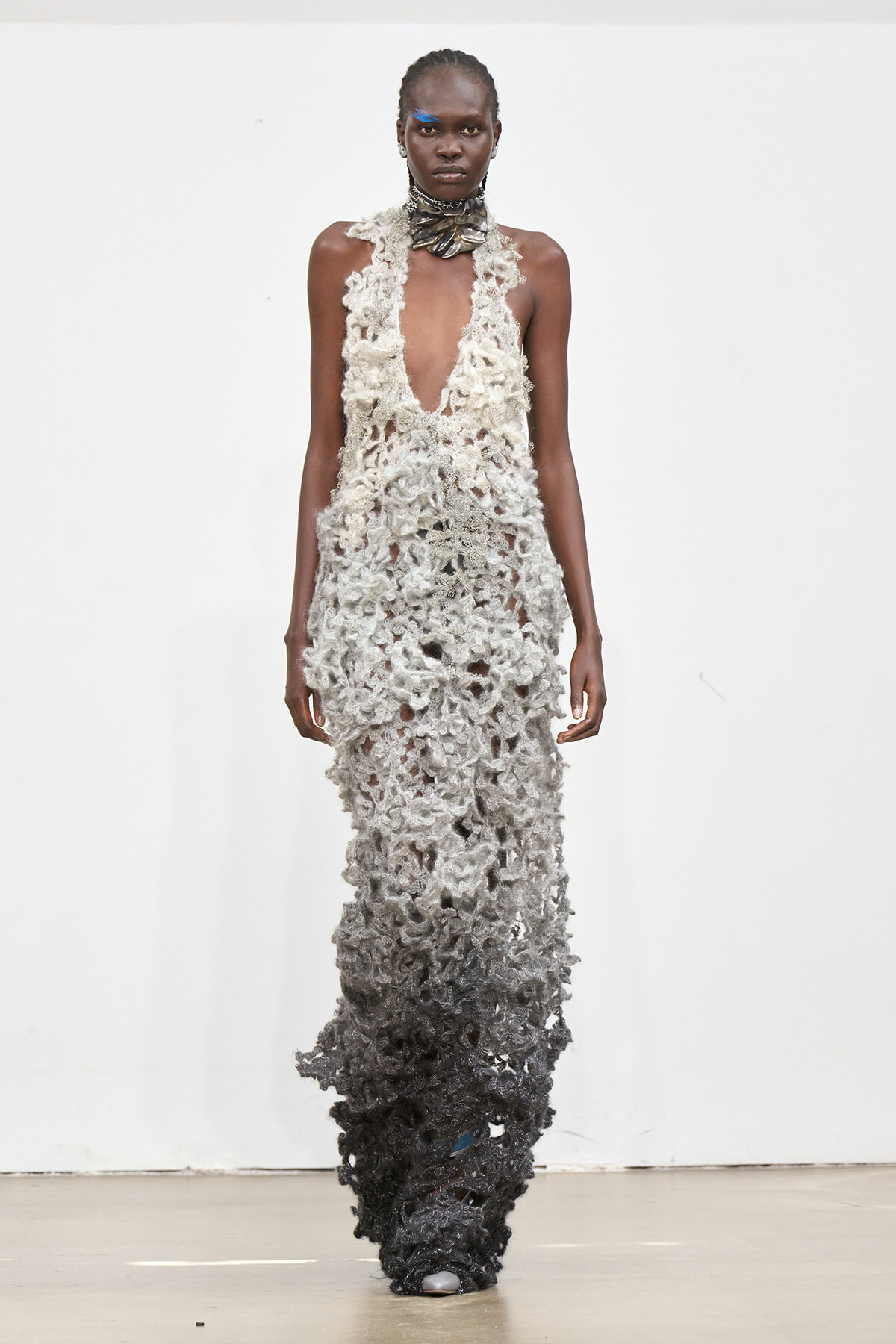 Model walks the runway in a sleeveless, floor-length lace gown that fades from cream at the top to black at the bottom with a textured, openwork pattern.