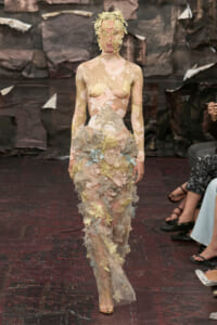 Model walking the runway in a sheer pastel floral lace gown with layered appliqués and a lace headpiece.