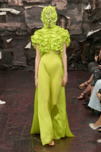 Model walking the runway in a neon lime gown with a voluminous ruffled top and matching leafy headpiece obscuring the face.