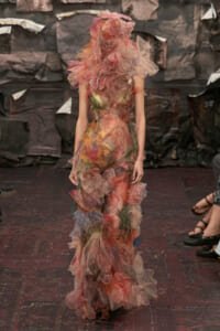 Runway model wearing a voluminous, multicolored tulle gown with pink ruffles and sheer, petal-like layers.