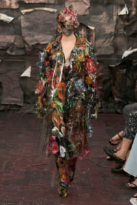 Model walks the runway in a transparent plastic coat covered with colorful leaves and flowers, with a matching plastic hood.