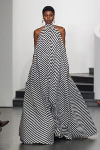 Woman wearing a black-and-white striped halter gown on a runway; bold chevron-like stripe pattern cascades to the floor.