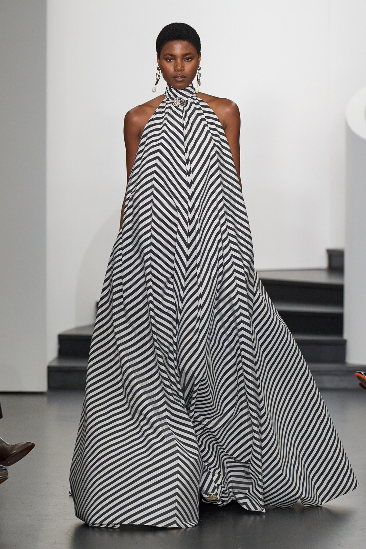 Woman wearing a black-and-white striped halter gown on a runway; bold chevron-like stripe pattern cascades to the floor.