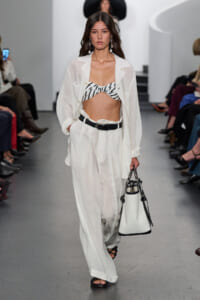Runway model in a white oversized suit with a zebra-print bandeau top, black belt, and a white and black handbag.