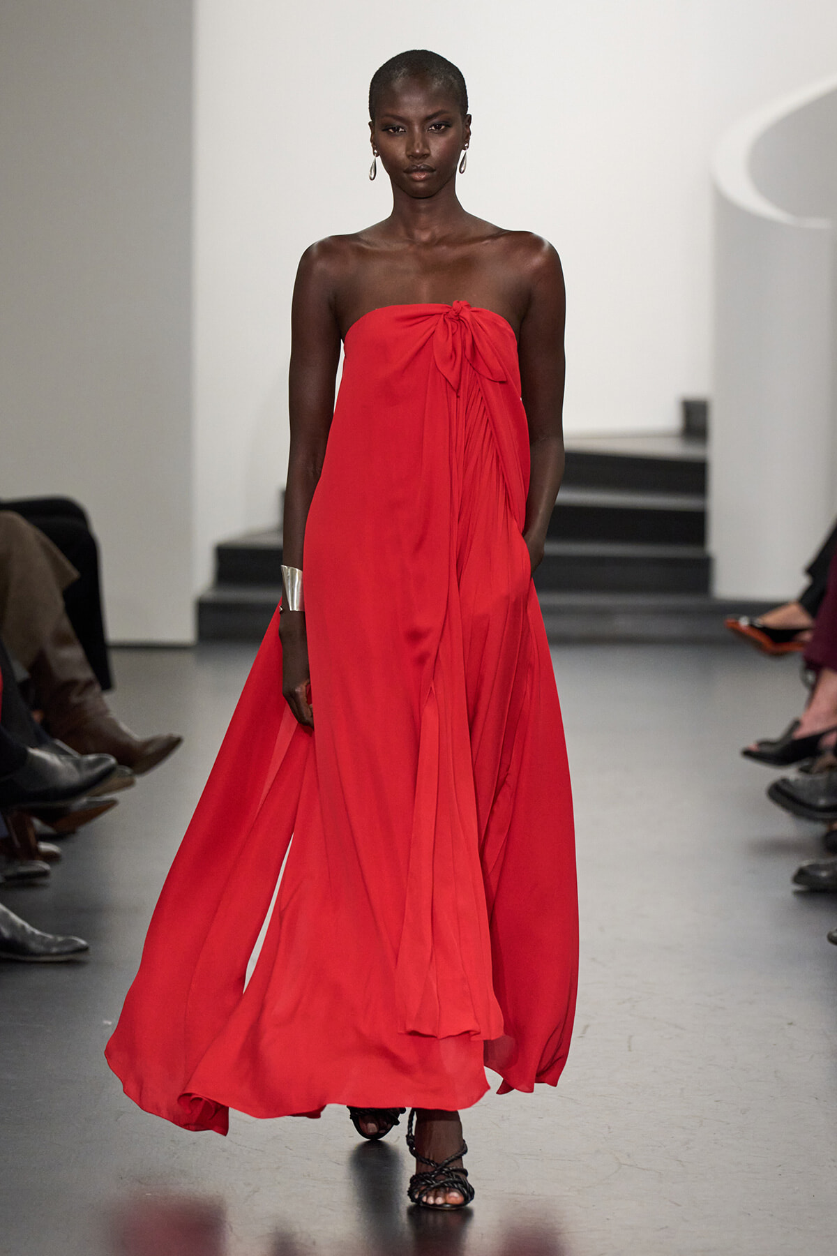 Model on a runway wearing a strapless red, floor-length gown with a knot at the bust and a flowing skirt.