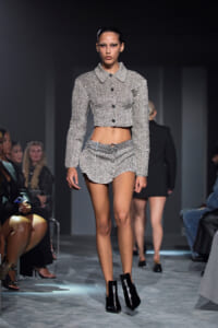 Model walks a silver textured cropped jacket and matching high-waisted shorts, black ankle boots on a runway.