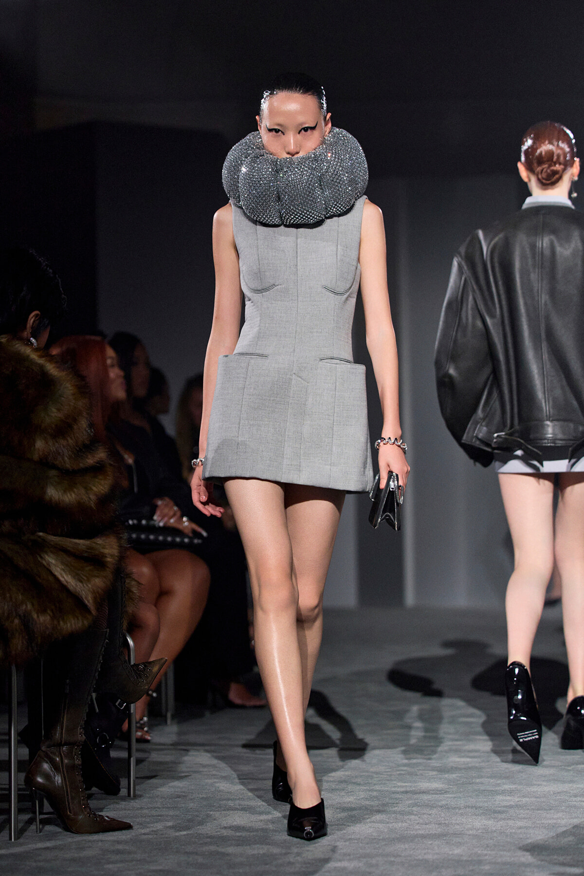 Runway model in a light gray sleeveless mini dress with a large sparkling beaded collar, walking the catwalk.