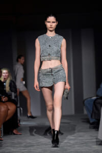 Model walks the runway in a silver textured sleeveless crop top and matching high-waisted shorts with a belt, holding a metallic clutch.