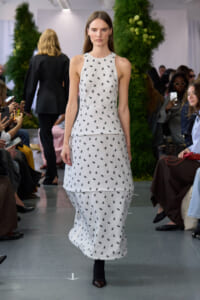 Model walks a white halter-neck midi dress with tiny black floral print on a runway.