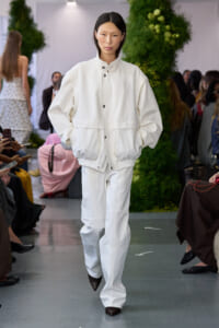 Model walks the runway in an oversized white jacket with a cinched waist and matching pants, during a fashion show.