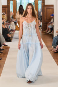 Model walks the runway in a pale blue, tiered maxi dress with an intricate white lace bodice.