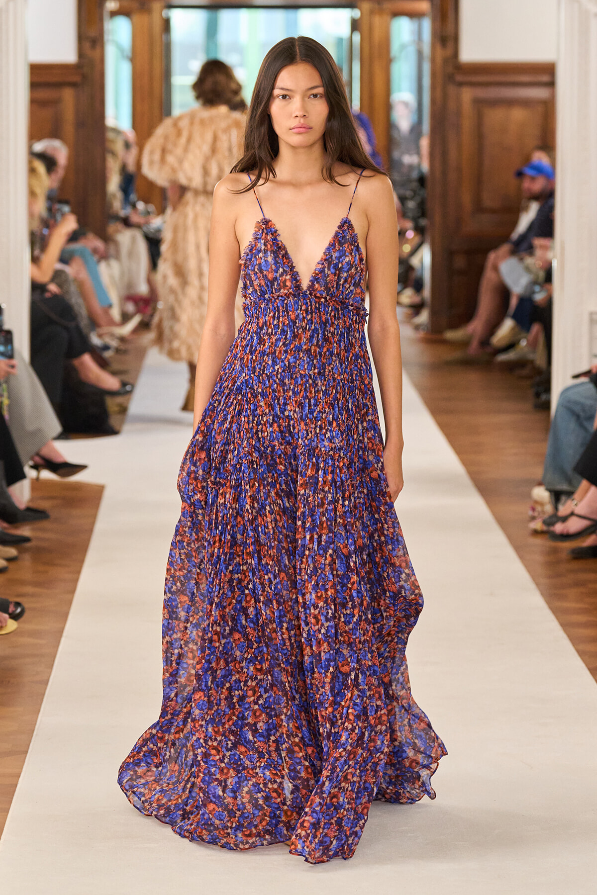 Model walks the runway in a blue and orange floral maxi dress with a plunging V neckline and thin straps.