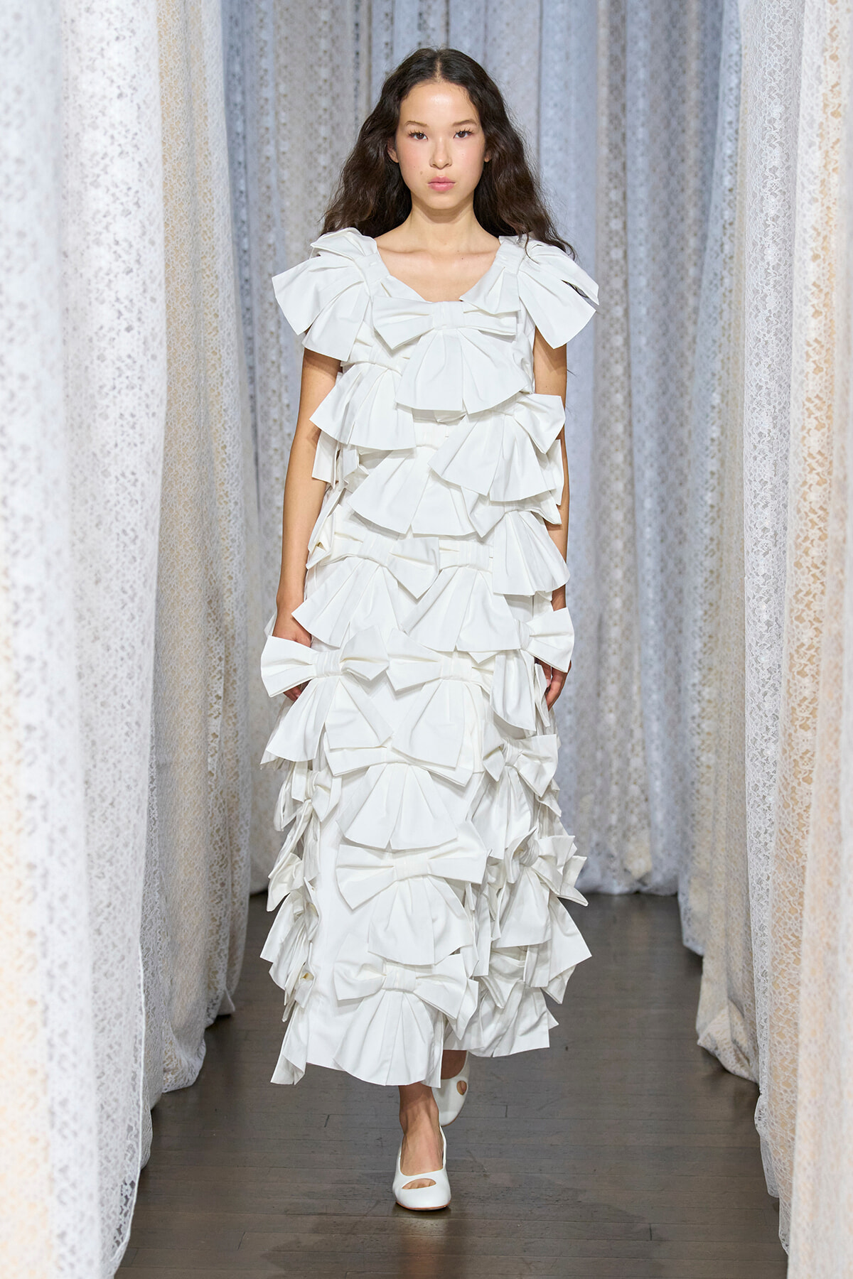 Model walking the runway in a white multi-tiered ruffled dress with oversized sleeves.