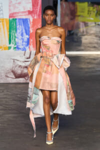 Runway model wearing a strapless pink patchwork dress with ruffle details and a voluminous, asymmetrical skirt.