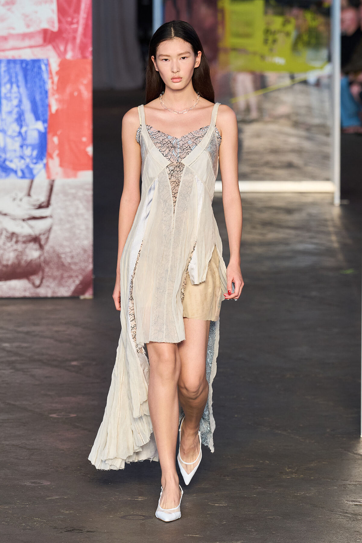 Female runway model wearing a cream lace and chiffon dress with a sheer overlay on the catwalk.