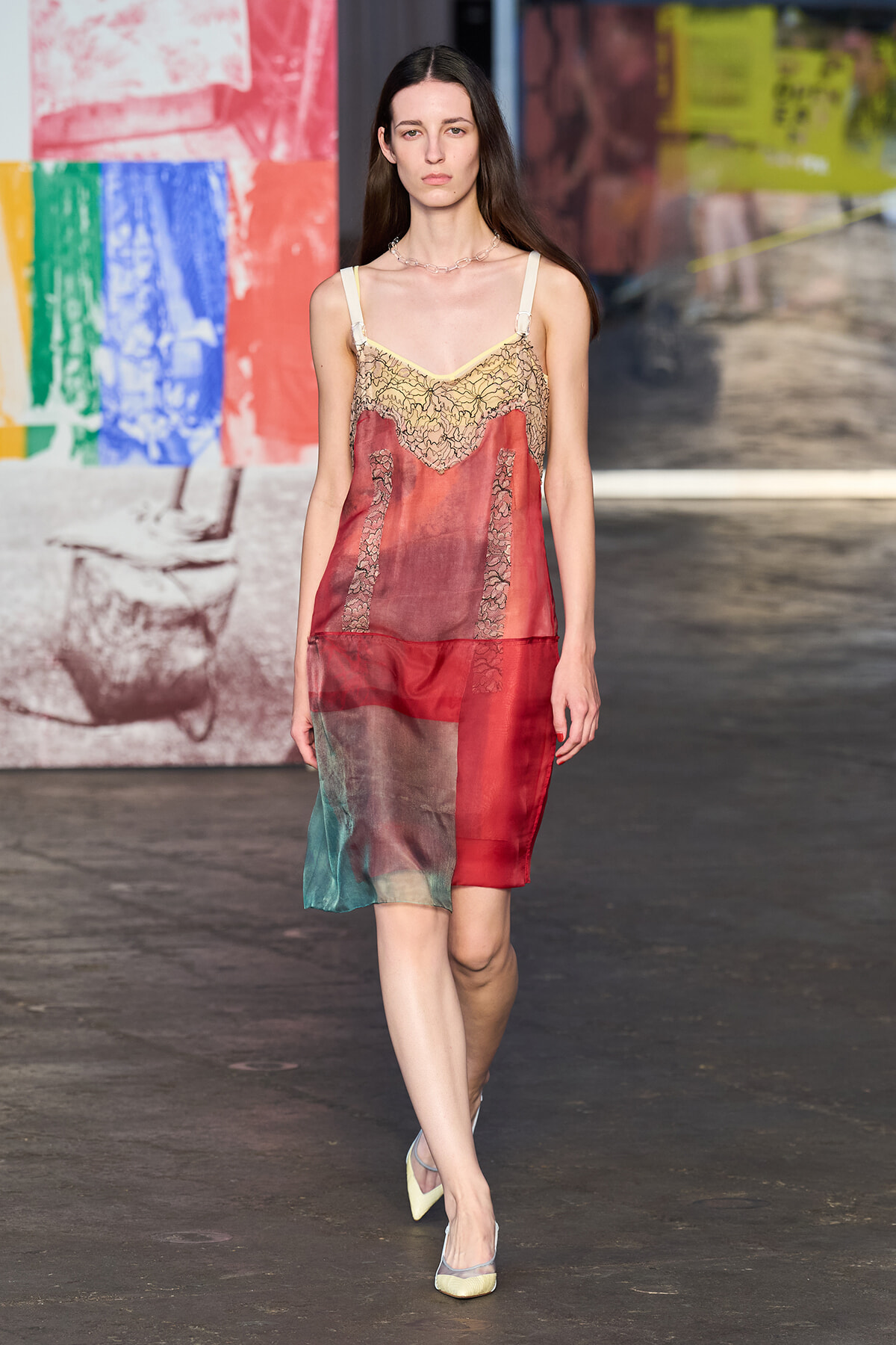 Model walking runway in a sheer color-block Slip dress with lace panels and pale straps, wearing yellow heels.