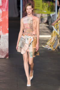 Runway model walking in a pastel patchwork mini skirt with a sleeveless peach top and white heels.