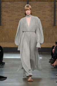 Model walks the runway in a heather gray, draped maxi dress with voluminous bishop sleeves and a matching belt/robe belt.