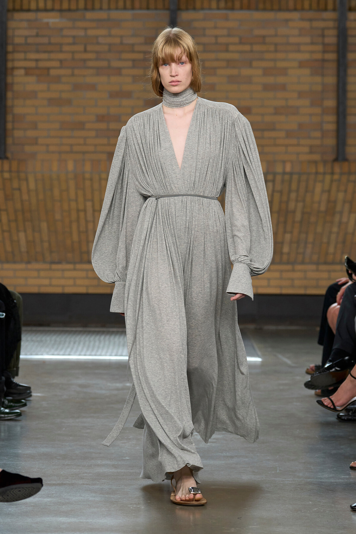 Model walks the runway in a heather gray, draped maxi dress with voluminous bishop sleeves and a matching belt/robe belt.