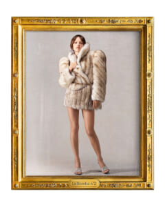 Model wearing a white fur coat with bare legs and silver sandals stands inside an ornate gold frame labeled La Bomba n°2, mid-pose for a high-fashion portrait.