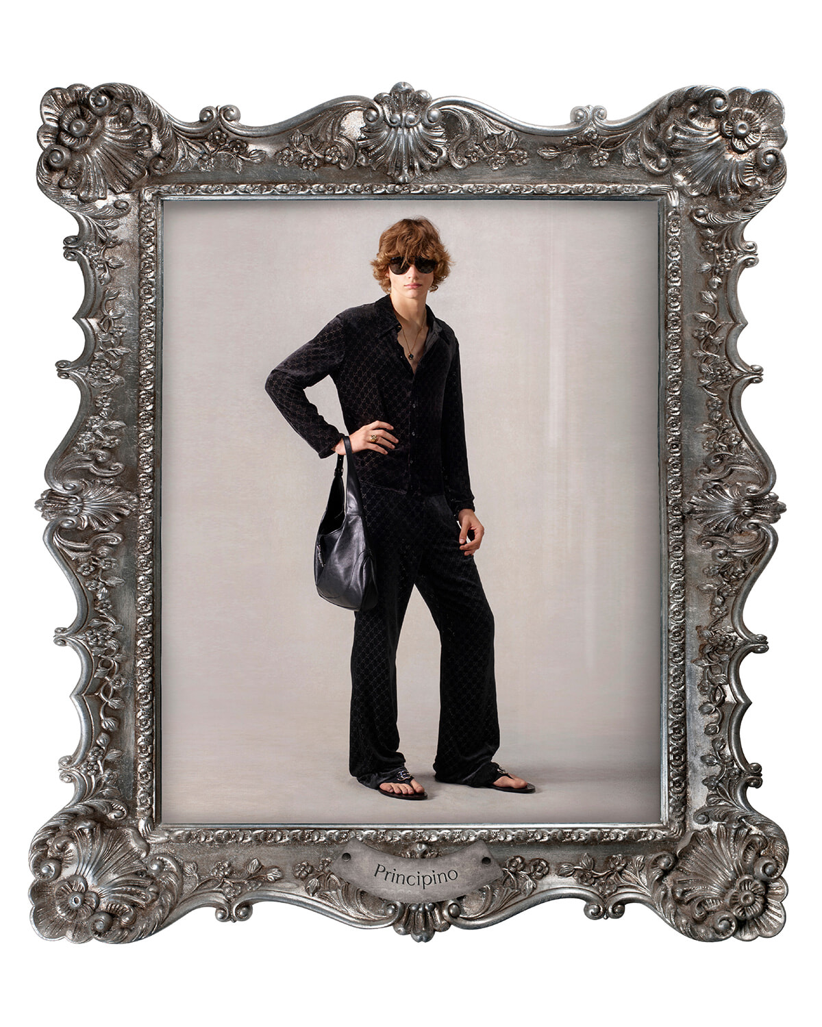 Model in a black quilted outfit with sunglasses and a black shoulder bag posing inside a large ornate silver frame labeled 'Principino'.