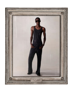 Framed portrait of a tall man in a black sequin tank top and trousers, wearing sunglasses, posing confidently.