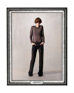 Male fashion model in a sheer black mesh shirt and matching sheer pants, hands in pockets, posed in a decorative frame labeled Androgino