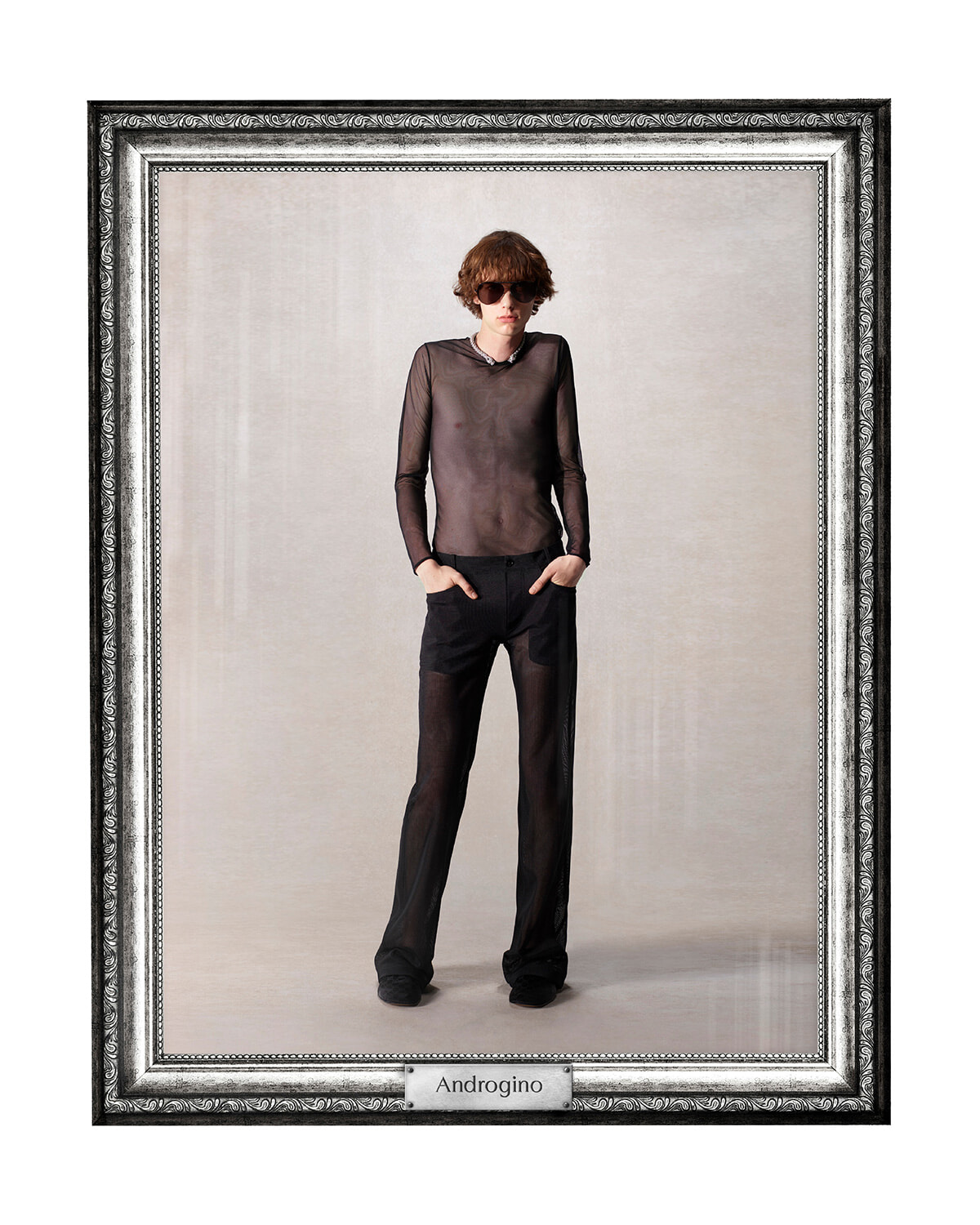 Male fashion model in a sheer black mesh shirt and matching sheer pants, hands in pockets, posed in a decorative frame labeled Androgino