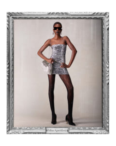 Model wearing a sparkly silver mini dress, black tights, sunglasses, and a silver clutch posing with hands on hips in a frame marked Miss Aperitivo