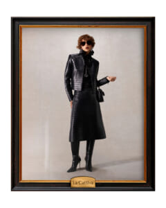 Framed fashion portrait of a woman in a black crocodile-skin coat and skirt, wearing sunglasses and holding a small black bag.