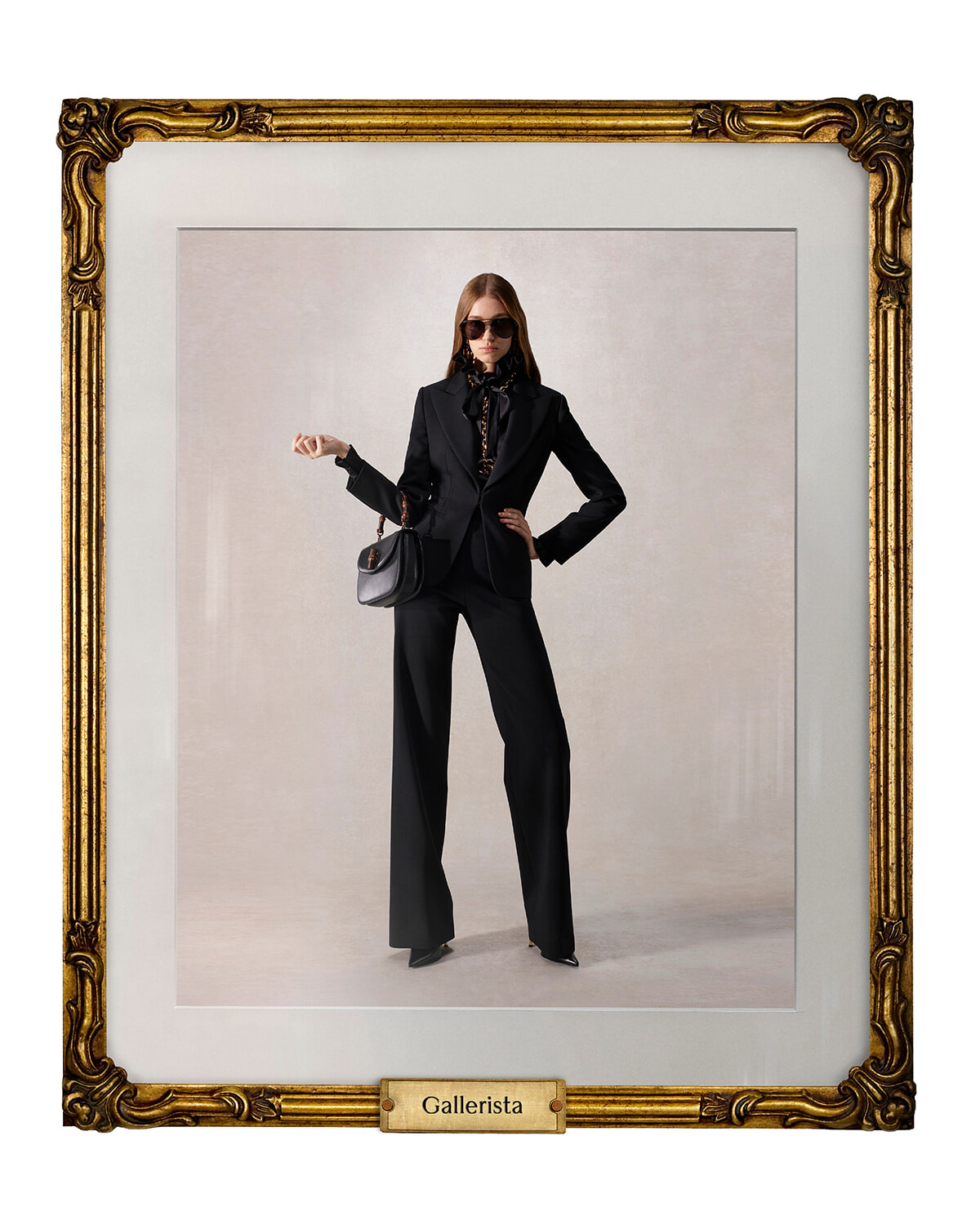 Model in a black pantsuit with sunglasses posing with a black handbag inside a gilded gallery frame labeled 'Gallerista'