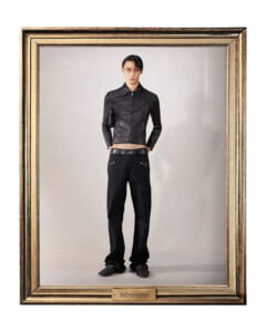 Male model in a black leather jacket and pants, standing with hands in pockets inside an ornate gold-framed portrait frame that reads 'Introverso' at the bottom plaque.